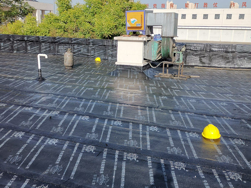 屋頂防水卷材鋪貼:清除基層表面雜物、油污、砂子，凸出表面的石子、砂漿疙瘩等應清理干凈，清掃工作必須在施工中隨時進行，并修補平整表面。尤其鏟除排水口、煙囪、管壁上的水泥砂漿等附著物；根據(jù)施工現(xiàn)場狀況，進行合理定位，確定卷材鋪貼方向，在基層上彈好卷材控制線，依循流水方向從低往高進行卷材試鋪。卷材試鋪后，先將要鋪貼的卷材剪好，反鋪于基面上(即是底部隔離紙朝上)，撕剝?nèi)ゾ聿母綦x紙。撕剝時，已剝開的隔離紙宜與粘結(jié)面保持45～60度的銳角，防止拉斷隔離紙，盡量保持在自然松弛狀態(tài)，但不要有皺折。