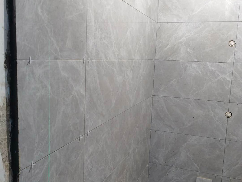 衛(wèi)生間貼磚施工：應(yīng)全部清理墻面上的各類污物，打掃干凈現(xiàn)場，特別是腳落里。用泥刀先批墻，后用水泥漿找平。這個工序很重要，確保底子平，防止貼后空鼓。墻面要刷防水涂料，防止貼后浸水，一般高度不低于1.8米，刷的時候會稍高一些。根據(jù)設(shè)計鋪貼圖樣的要求，確定排磚方案，用墨斗彈線，以減少施工損耗。把剛剛攪拌好的粘結(jié)劑漿料均勻的刮到墻上。瓷磚上墻將經(jīng)過預(yù)先清潔的瓷磚平整地鋪貼在粘結(jié)劑漿料基層上，使用橡膠錘將瓷磚拍實鋪平。施工過程中，可小幅度轉(zhuǎn)動瓷磚，使?jié){料與瓷磚背面充分接觸。專家建議在鋪貼時，隨機取下已鋪貼于基層上的瓷磚作檢查。確保漿料與瓷磚背面的充分接觸。 留縫大小調(diào)整根據(jù)瓷磚的尺寸，在磚與磚之間預(yù)留相應(yīng)尺寸的縫隙留待嵌縫。可用牙簽等先固定，粘結(jié)劑具有一定的可調(diào)整性，可對留縫的大小進行調(diào)整。