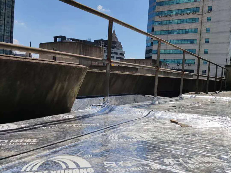 屋頂防水卷材鋪貼:1、由于設(shè)計(jì)要求屋面找坡層按2％坡度放坡，因此卷材鋪設(shè)時(shí)應(yīng)平行于屋脊自下而上的鋪貼，卷材搭縫必須嚴(yán)密，縫口應(yīng)順?biāo)鞣较虼罱?，其寬度不?yīng)小于50mm，上下屋接縫應(yīng)左右錯(cuò)開250mm，在鋪大面積防水卷材之前，應(yīng)將檐溝，管道口、雨水口處的附加防水布鋪好后由屋頂?shù)牡吞幭蚋咛庍M(jìn)行大面積的鋪貼。 2、屋頂卷材遇到女兒墻時(shí)，應(yīng)將卷材沿墻上卷，高度應(yīng)低于250mm，然后固定在墻上預(yù)埋的木磚和木塊上，并用1：3水泥砂漿做坡水。 3、凡管道等伸出屋面的構(gòu)件必須在屋頂上開孔時(shí)，為了防漏水應(yīng)將卷材向上翻起，抹以水泥砂漿或再蓋上鍍鋅鐵皮起擋水作用，泛水高度不超過200mm。 防水材料卷材層應(yīng)粘結(jié)牢固，無空鼓、損傷、滑移，翹邊、起泡、皺折等缺陷。防水工程施工完畢后，必須作蓄水試驗(yàn)合格后開始進(jìn)行下道工序。