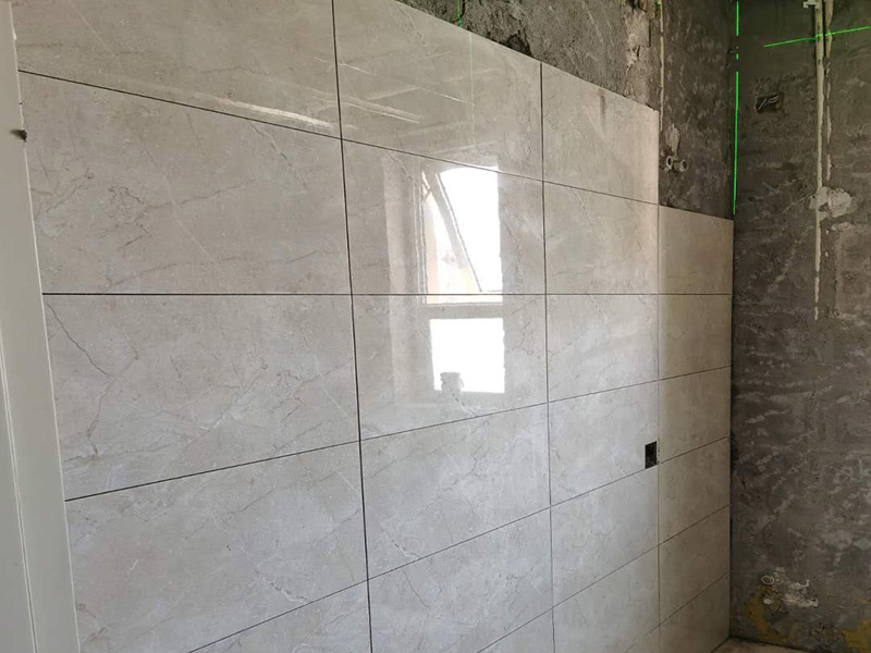 客廳瓷磚鋪貼:鋪貼前，先將所鋪平面表面的塵土、雜物等徹底清掃干凈，平面不能有空鼓、開裂和起砂等現(xiàn)象，如果存在這些現(xiàn)象，要先進行修復(fù)處理，在鋪設(shè)瓷磚。鋪設(shè)地磚施工前，要先在地面彈出十字線，從而控制地磚分隔尺寸。然后要選用1:3干硬性水泥砂漿，砂漿的厚度要在25mm左右。把瓷磚按照要求放在水泥砂漿上，用橡皮錘輕輕敲擊瓷磚的表面，直至瓷磚鋪貼平整。鋪貼完瓷磚后，要進行勾縫處理，先清理干凈瓷磚縫隙里的雜質(zhì)，再用專用填縫劑進行勾縫處理。