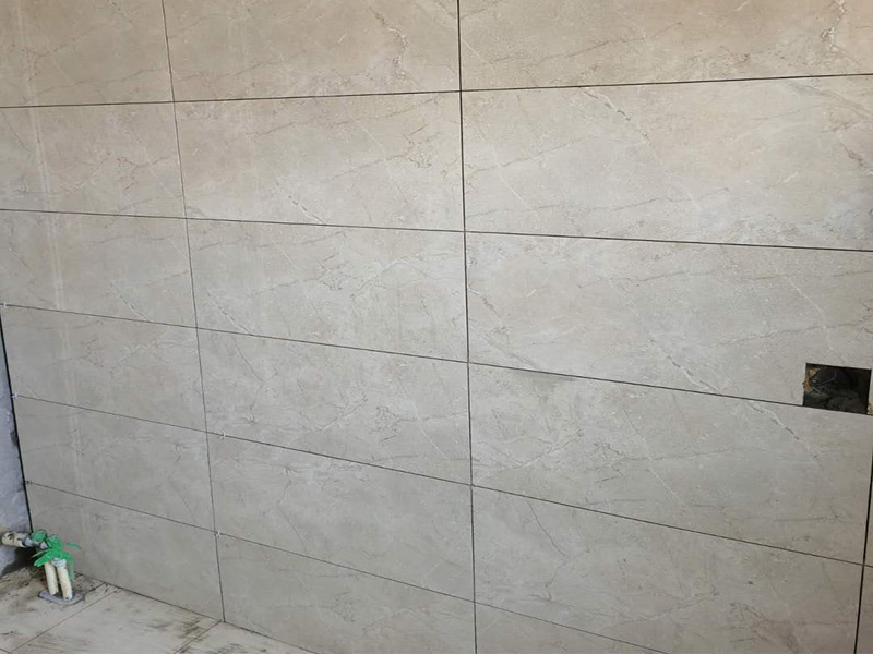 客廳瓷磚鋪貼:鋪貼前，先將所鋪平面表面的塵土、雜物等徹底清掃干凈，平面不能有空鼓、開裂和起砂等現(xiàn)象，如果存在這些現(xiàn)象，要先進行修復(fù)處理，在鋪設(shè)瓷磚。鋪設(shè)地磚施工前，要先在地面彈出十字線，從而控制地磚分隔尺寸。然后要選用1:3干硬性水泥砂漿，砂漿的厚度要在25mm左右。把瓷磚按照要求放在水泥砂漿上，用橡皮錘輕輕敲擊瓷磚的表面，直至瓷磚鋪貼平整。鋪貼完瓷磚后，要進行勾縫處理，先清理干凈瓷磚縫隙里的雜質(zhì)，再用專用填縫劑進行勾縫處理。