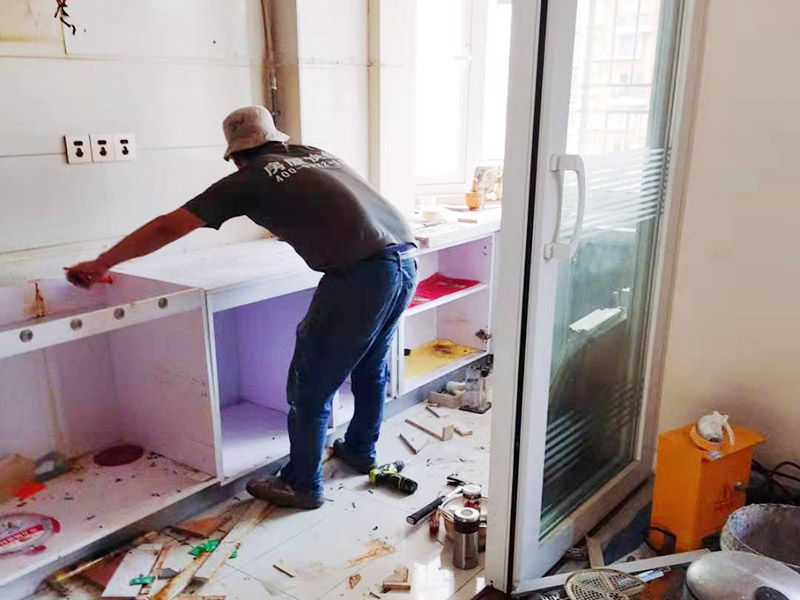 廚房櫥柜安裝：清理：對(duì)廚房作防護(hù)措施，掛擋布、廚房墻面等做簡(jiǎn)單清理，以便準(zhǔn)確測(cè)量地面水平。櫥柜安裝一般先從地柜開(kāi)始。把櫥柜外包裝拆開(kāi)后。在櫥柜的邊緣貼上防火膜封邊。在下柜底部安裝上支腳，根據(jù)地面水平高度調(diào)整櫥柜。 櫥柜安裝需要找出基準(zhǔn)點(diǎn)，L型廚房從直角處向兩邊延伸，U型廚房則先將中間的一字型柜體放整齊后，再?gòu)膬蓚€(gè)直角處向兩邊站看，這樣可以避免出現(xiàn)縫隙。櫥柜框架安裝牢固定位后，需要在櫥柜背面安裝背板。一般安裝下水都會(huì)現(xiàn)場(chǎng)開(kāi)孔，工人會(huì)用專(zhuān)業(yè)的打孔器按照管道大小進(jìn)行打孔，打孔的直徑應(yīng)比管道大3-4毫米，并且打孔后要將開(kāi)孔部分用密封條封邊，防止邊緣滲水木材變形。